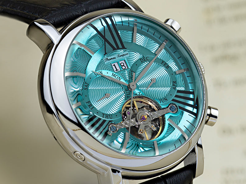 Thomas Tompion Whitefrairs Watch with black strap, silver casing and light blue dial. The watch has a open heart dial showing the mechanism and has two subdials with the days of the week and months on the watch face.